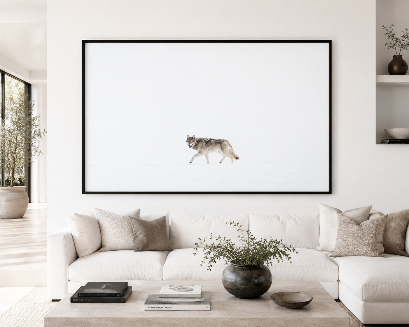 Framed print of a lone wolf walking across a vast snowfield, hung above a linen sofa in a bright minimalist living room