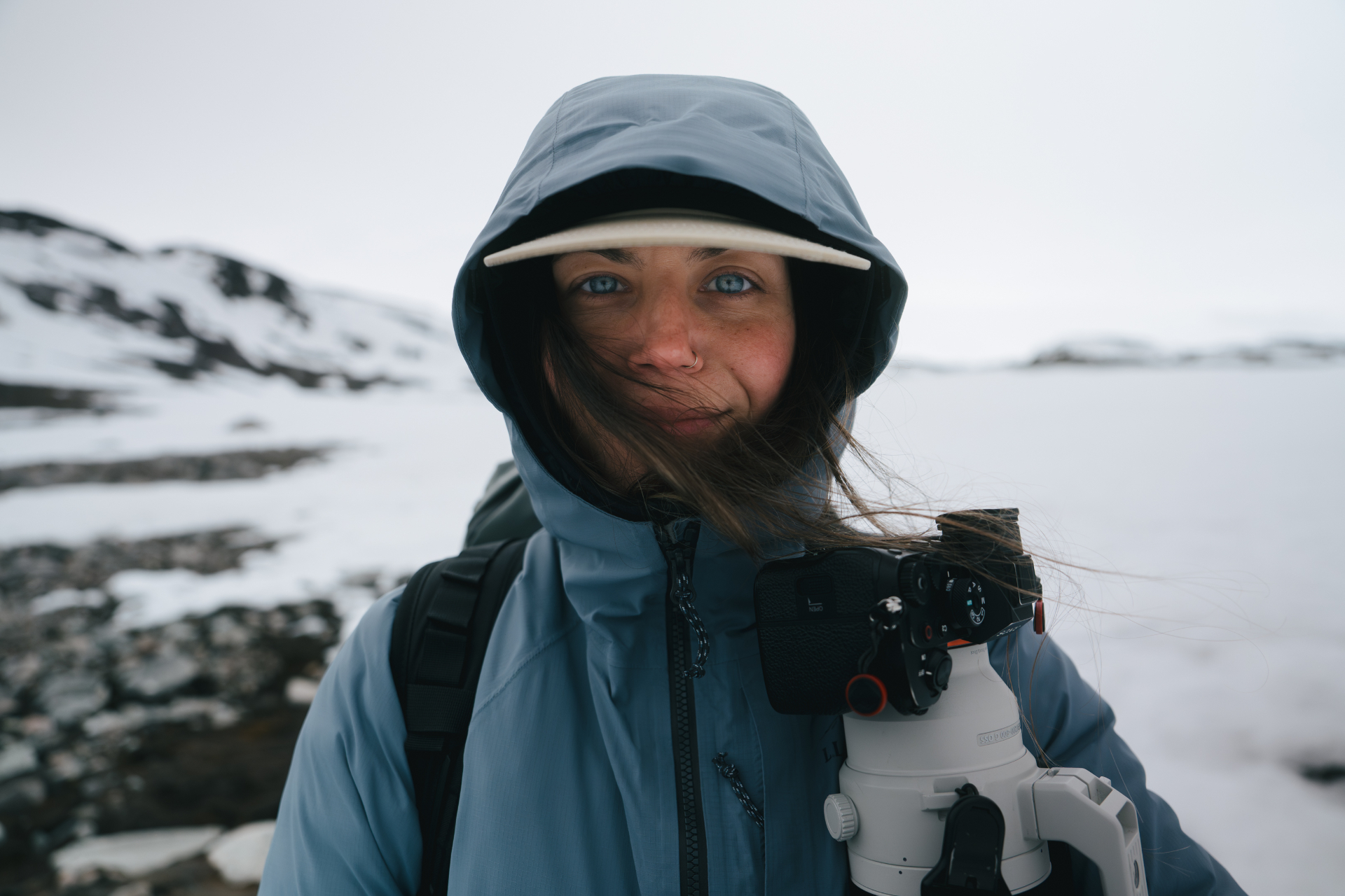 Hannah in a blue hooded jacket and hat, holding a camera in a snowy arctic landscape